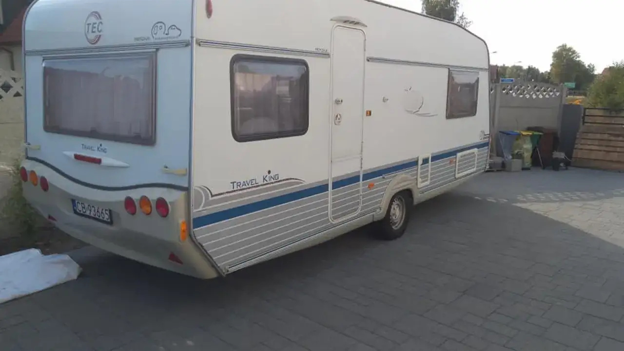 Biała przyczepa kempingowa TEC Travel King z niebieskimi pasami, gotowa na wakacyjne podróże.