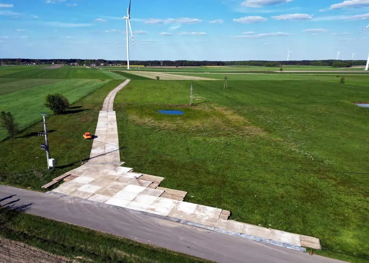 Teren budowy farmy wiatrowej z tymczasową drogą z płyt betonowych. Tłuczeń na drodze ułatwia dojazd ciężkiego sprzętu.