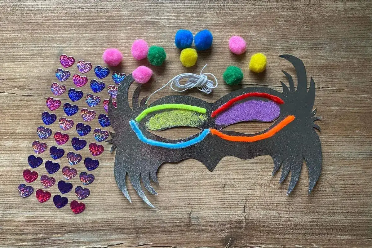 Materiały do stworzenia maski karnawałowej: srebrna baza, kolorowe pompony, brokatowe serduszka, druciki kreatywne i sznurek.