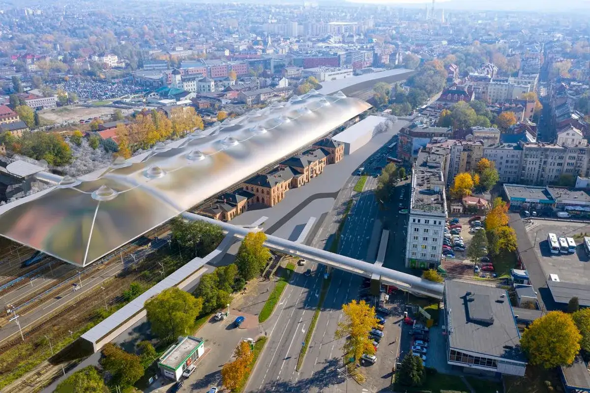Widok z lotu ptaka na nowoczesny dworzec kolejowy z falistym dachem i zabytkowymi budynkami.
