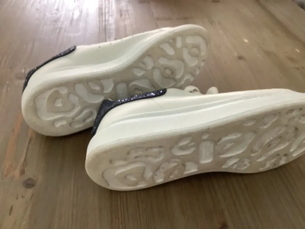 Białe sneakersy Alexander McQueen z granatowymi brokatowymi wstawkami. Zwróć uwagę na charakterystyczną podeszwę, by jak rozpoznać oryginalne buty Alexander McQueen.