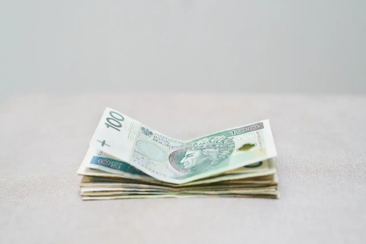 Stos polskich banknotów, w tym 100 zł, leży na jasnym tle. Zastanawiamy się, ile RMF zarabia na loterii.