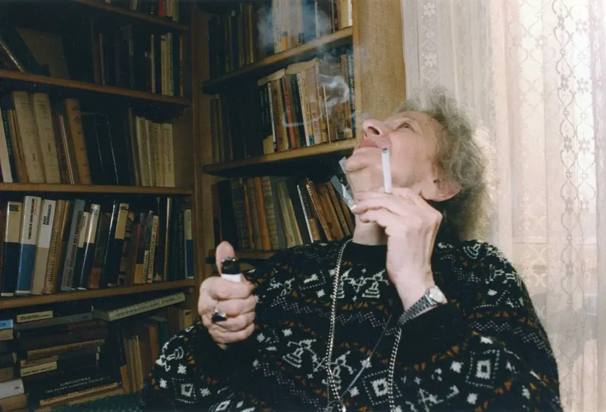 Wisława Szymborska, zapalając papierosa, otoczona książkami. Ciekawe, o czym myślała?