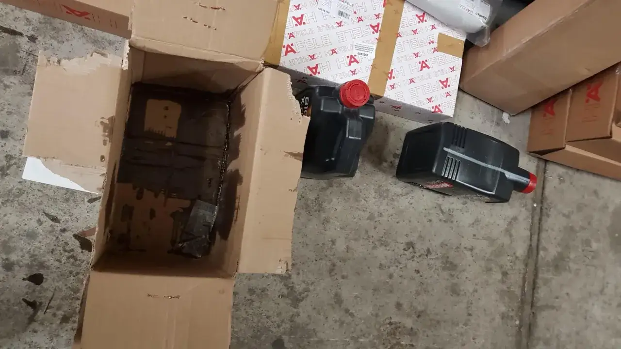 Otwarty karton z ciemnym płynem i dwa czarne kanistry z olejem silnikowym Motul.