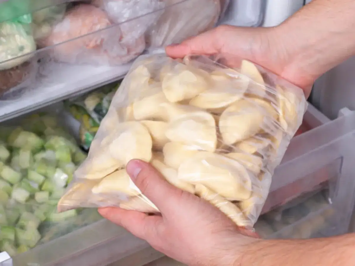 Ręce wkładają do zamrażarki worek z pierogami. To prosty sposób, jak mrozić pierogi, by cieszyć się nimi później.