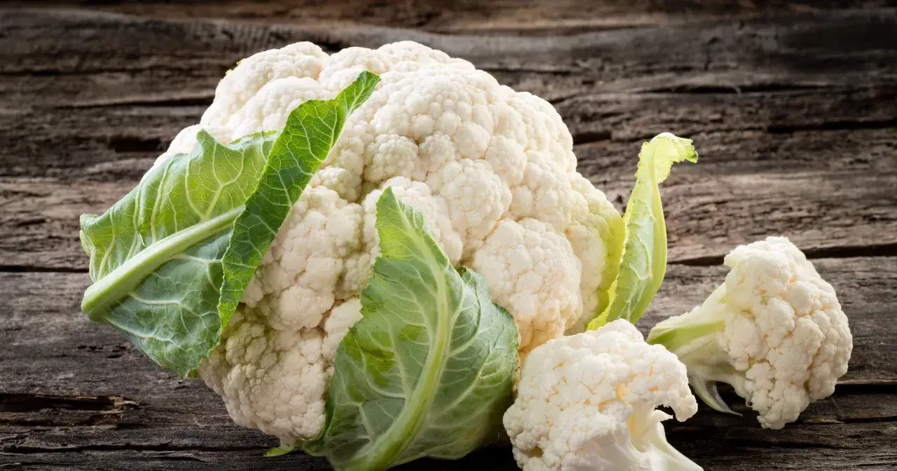 Świeży kalafior z zielonymi liśćmi na drewnianym tle. Czy kalafior jest dietetyczny? Tak, to warzywo niskokaloryczne.