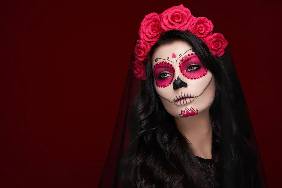 Kobieta z makijażem sugar skull, ozdobiona różami i welonem. Przerażające makijaże na Halloween w pełnej krasie.