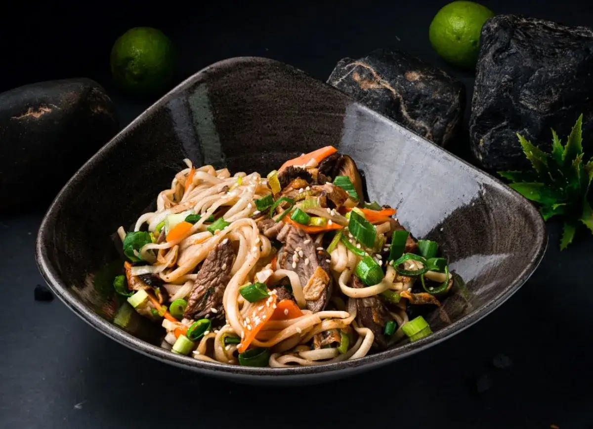 Miseczka pełna pysznego pad udon z wołowiną, warzywami i szczypiorkiem, ozdobiona sezamem.