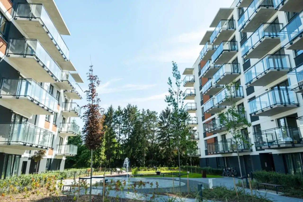 Nowoczesne bloki mieszkalne z balkonami i zielonym dziedzińcem.