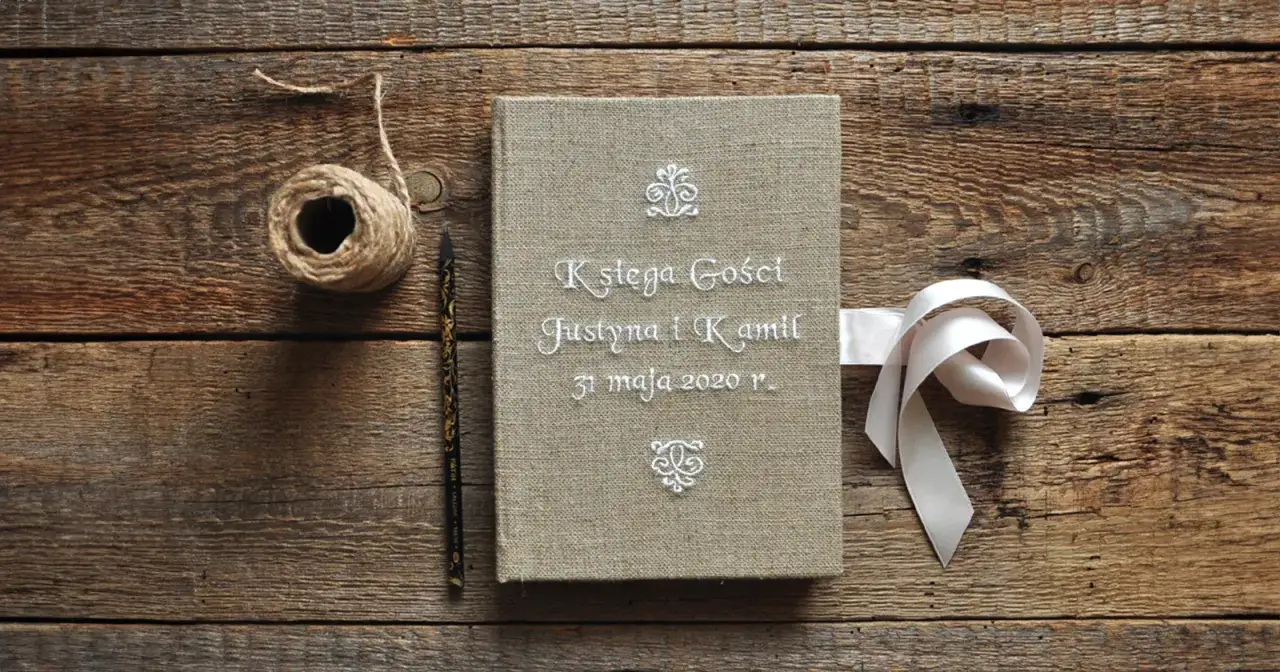 Oto pomysł co zamiast księgi gości na weselu: lniana księga z imionami Justyny i Kamila, ozdobiona wstążką.
