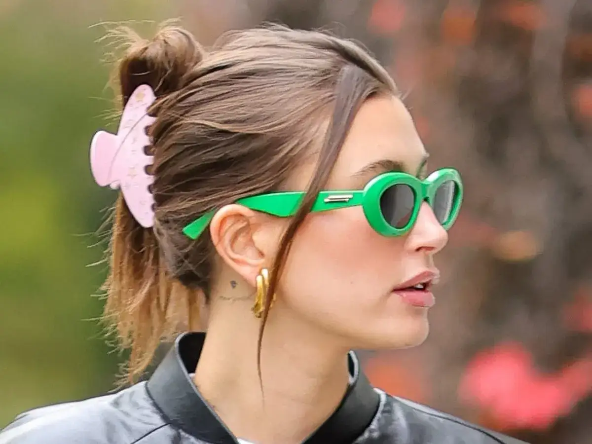 Kobieta z różową klamrą we włosach i zielonymi okularami przeciwsłonecznymi.
