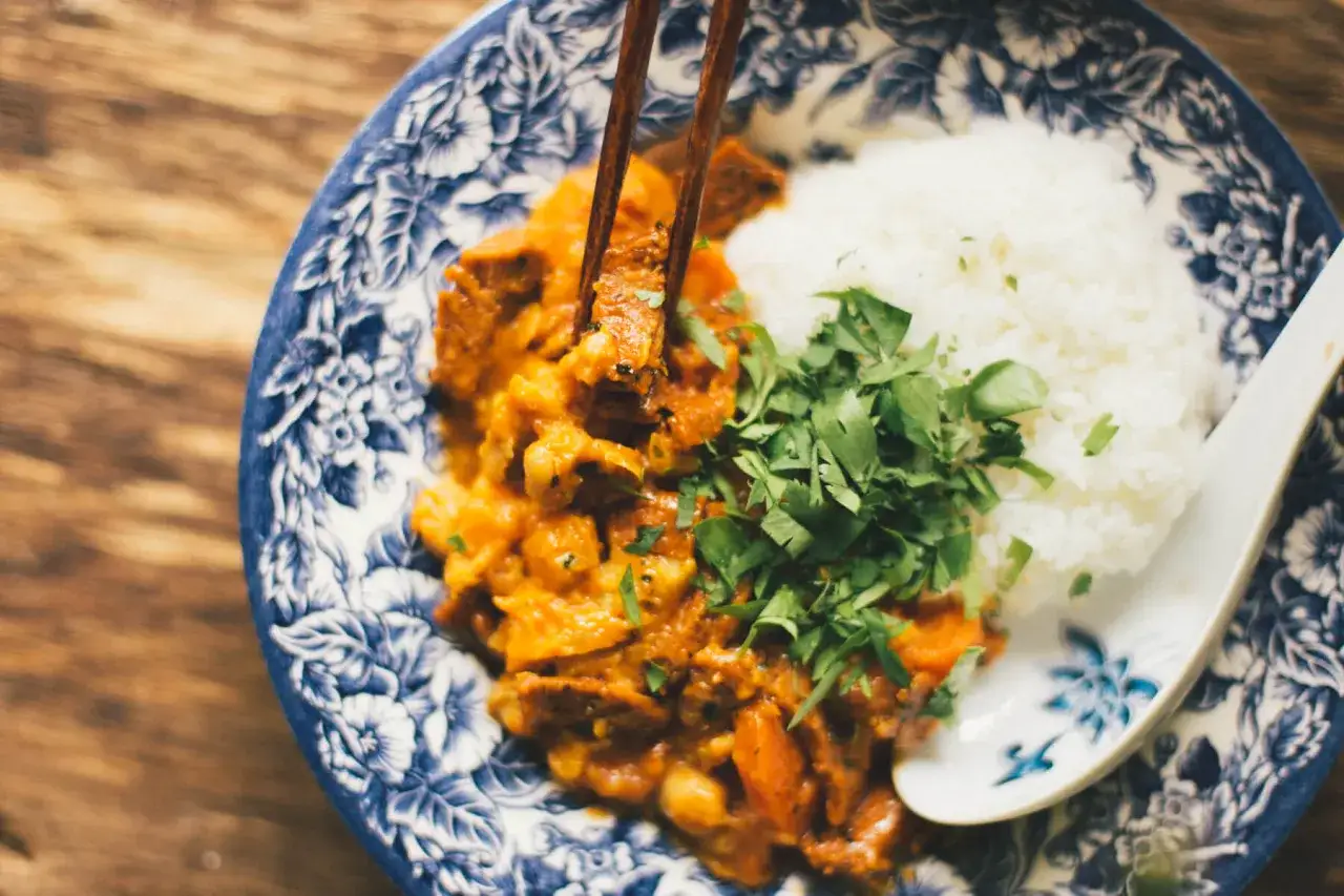 Miseczka z ryżem i curry, podana z posiekaną natką pietruszki, jedzona pałeczkami.