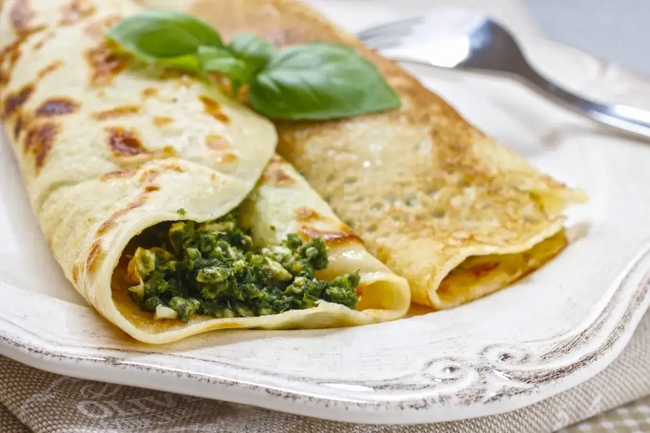 Naleśniki ze szpinakiem, idealne gdy zastanawiasz się, jak przyrządzić szpinak mrożony. Podane z listkiem bazylii.