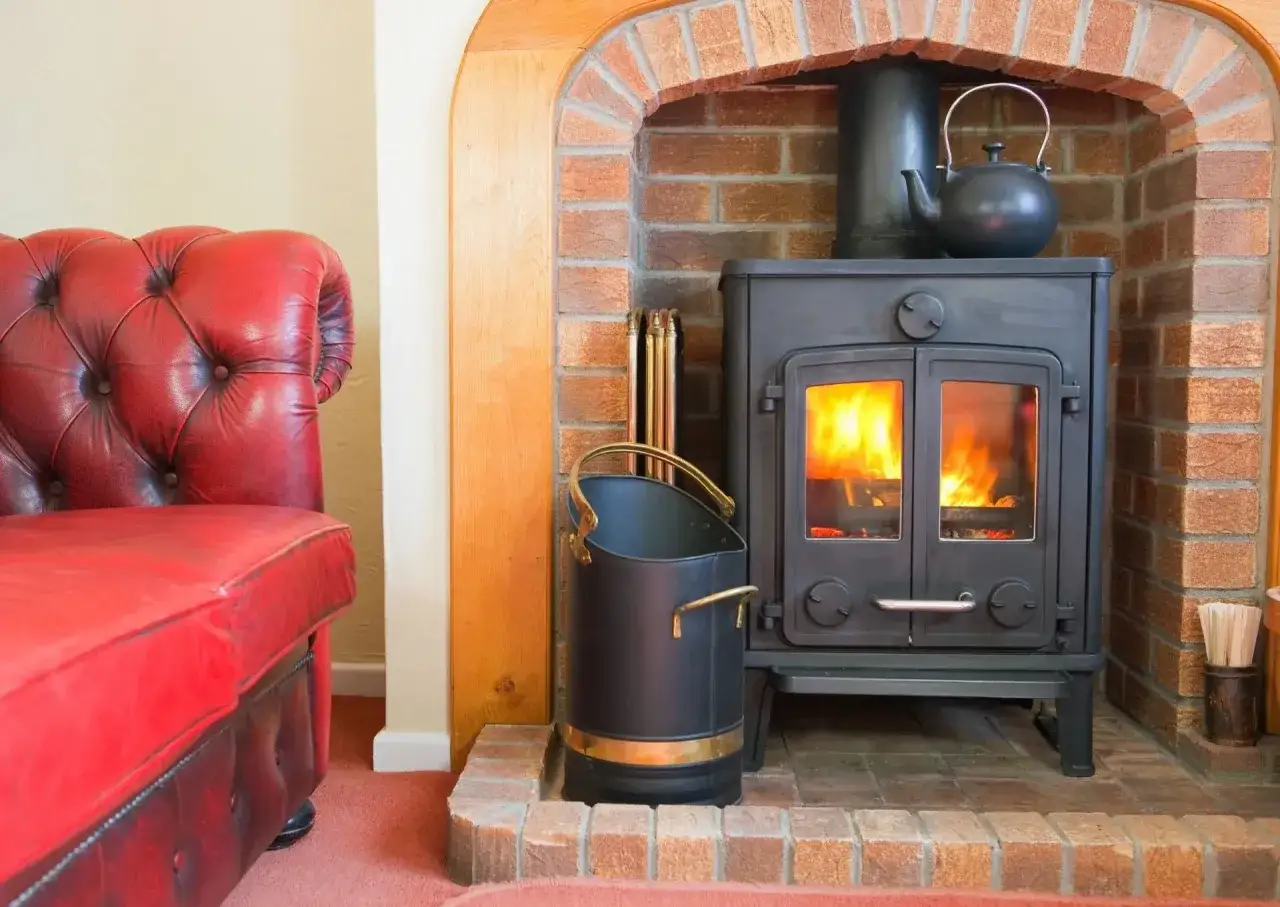 Czerwona kanapa i palący się piecyk zapewniają przytulne ogrzewanie domku letniskowego. Czajniczek na piecu dodaje uroku.