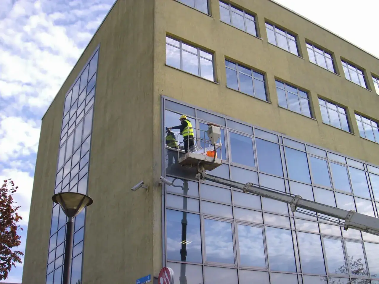 Pracownicy na podnośniku montują okno w nowoczesnym budynku.