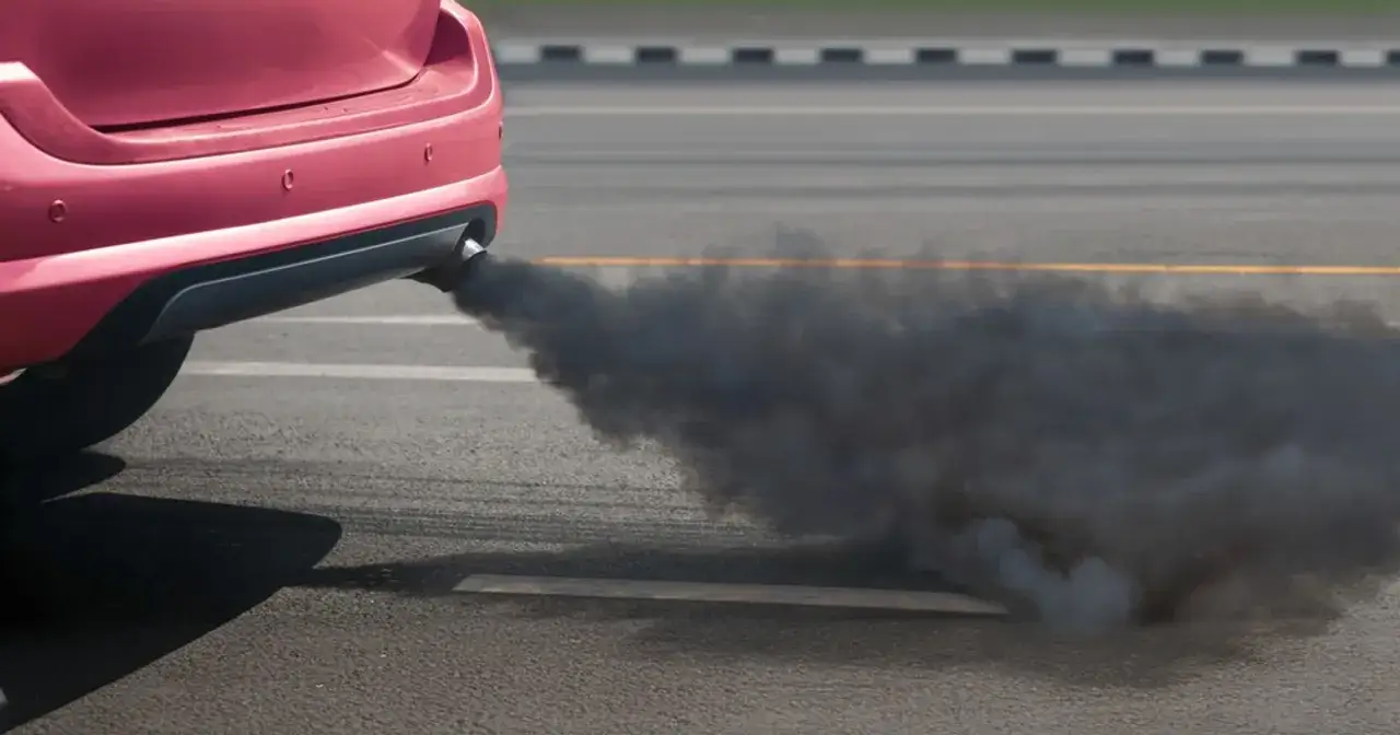 Czerwony samochód z rury wydechowej wydobywa się gęsty, czarny dym.