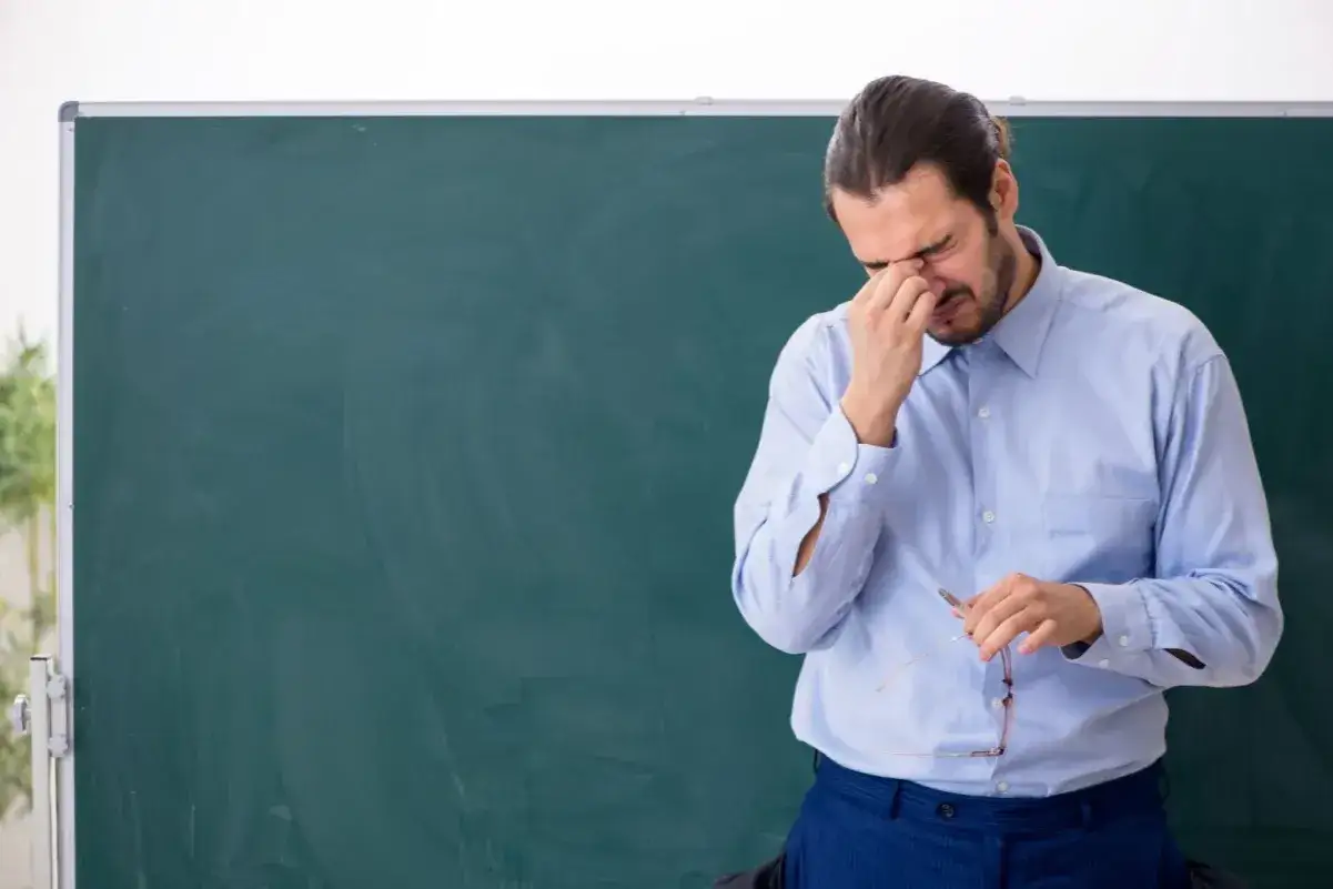 Nauczyciel z bólem głowy, trzymający okulary, zmęczony po całym dniu pracy. Dodatek za wychowawstwo chyba nie rekompensuje tego stresu.