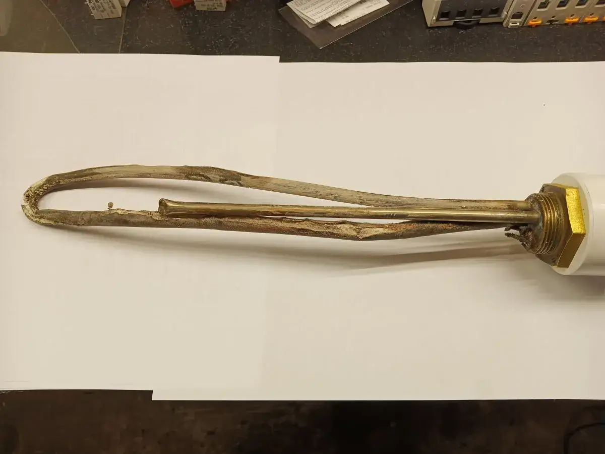 Zużyta, skorodowana grzałka elektryczna bojlera z osadem kamienia.