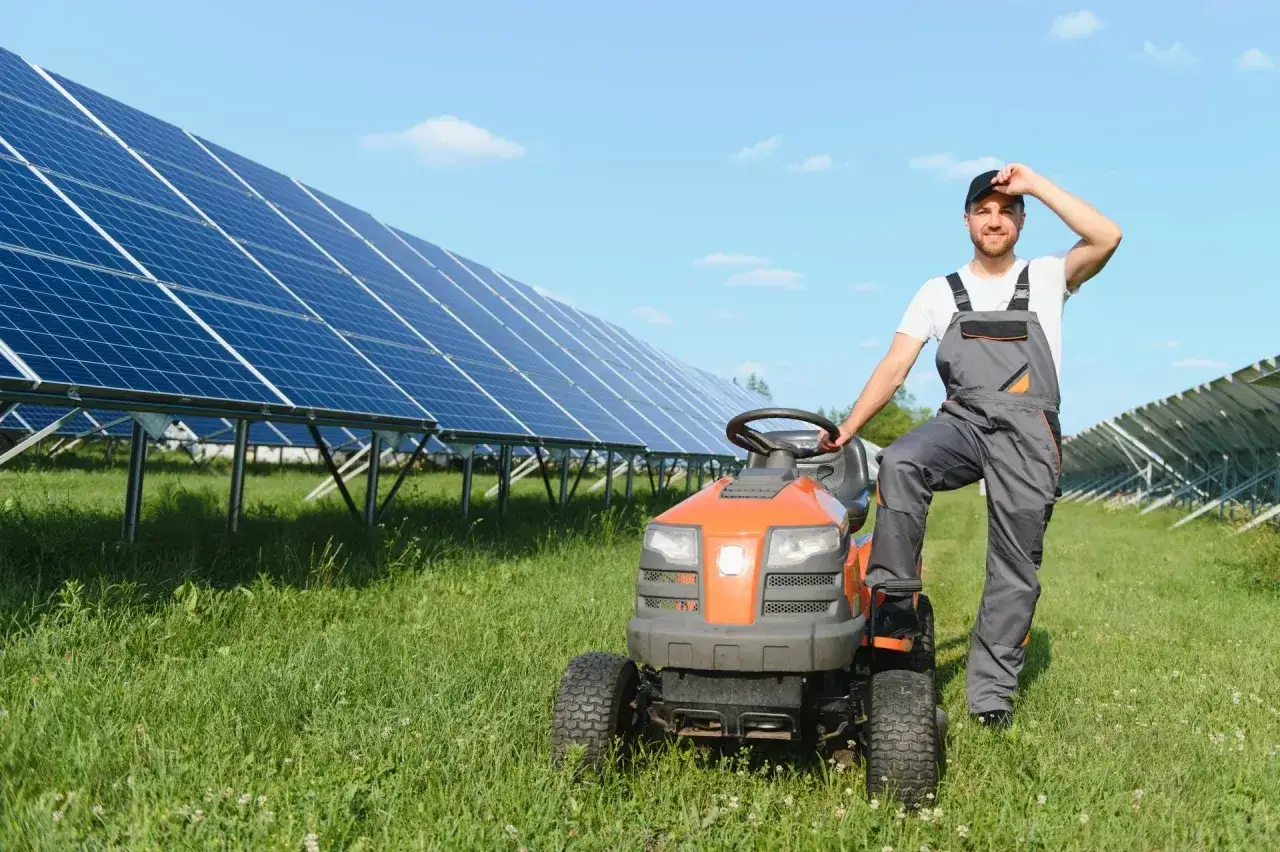Rolnik w ogrodniczkach odpoczywa przy traktorku, obok rzędy paneli słonecznych zapewniających czystą energię dla wsi.