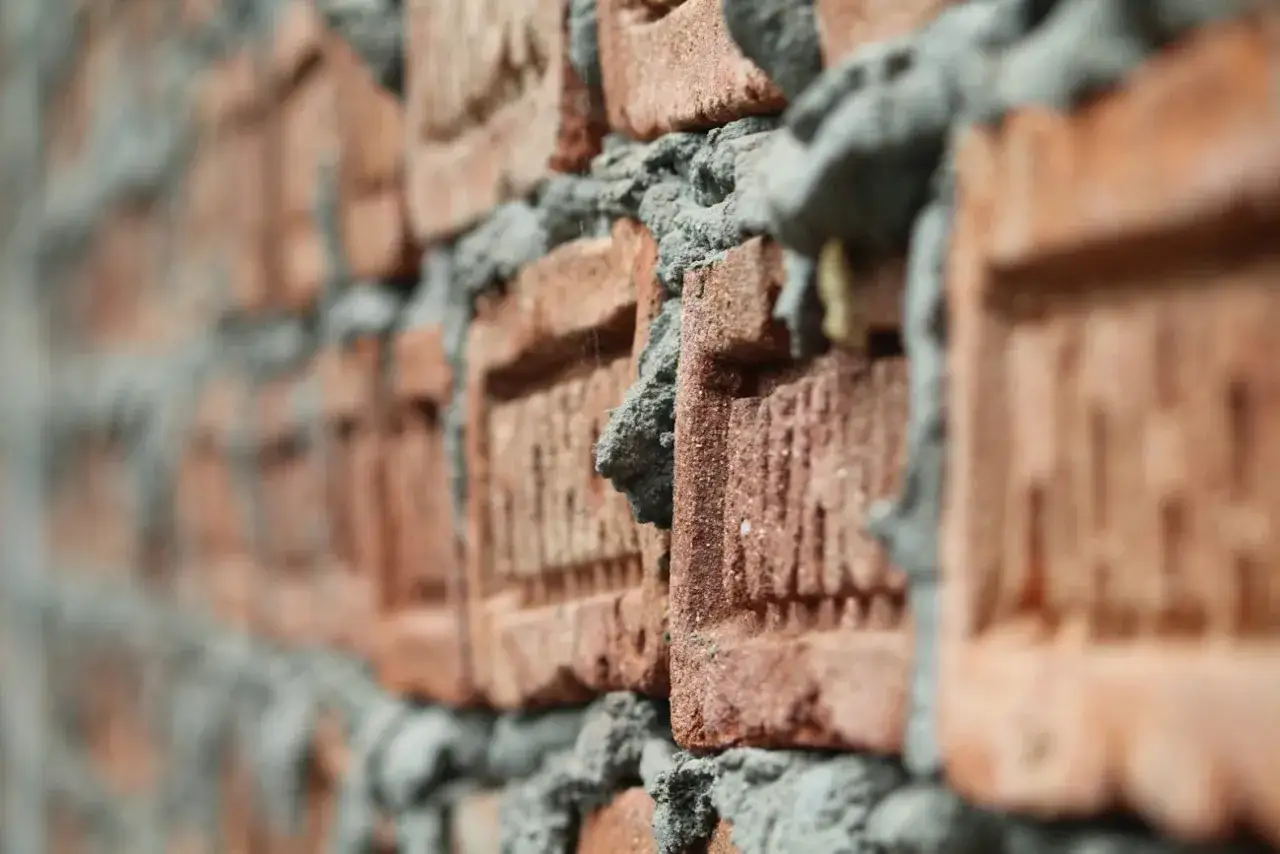 Zbliżenie na ceglaną ścianę w budowie. Widać nierównomierne spoiny zaprawy, sugerujące proporcje zaprawy tynkarskiej na łopaty.
