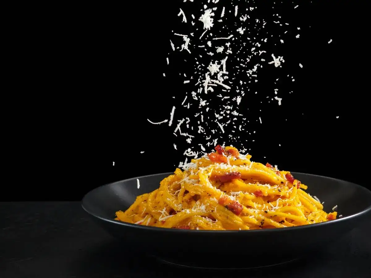 Ser do carbonary sypie się na talerz z makaronem.