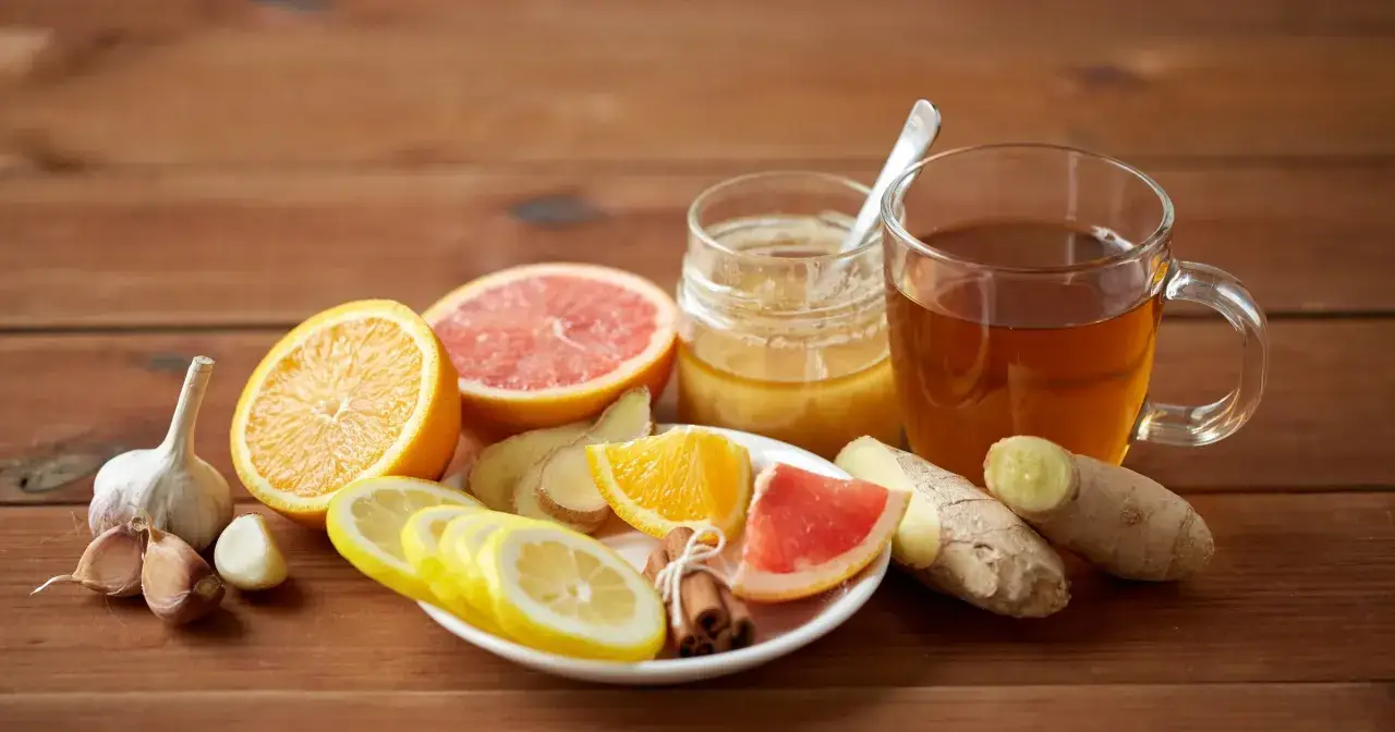 Herbata z imbirem, cytryną, pomarańczą, grejpfrutem, miodem i czosnkiem na drewnianym tle.