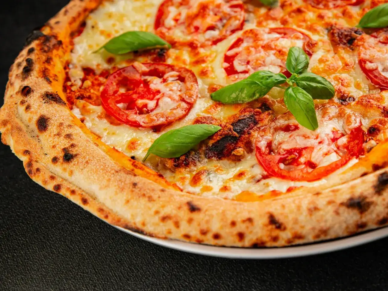 Zbliżenie na pizzę margherita z pomidorami, mozzarellą i bazylią, z przypieczonymi brzegami.
