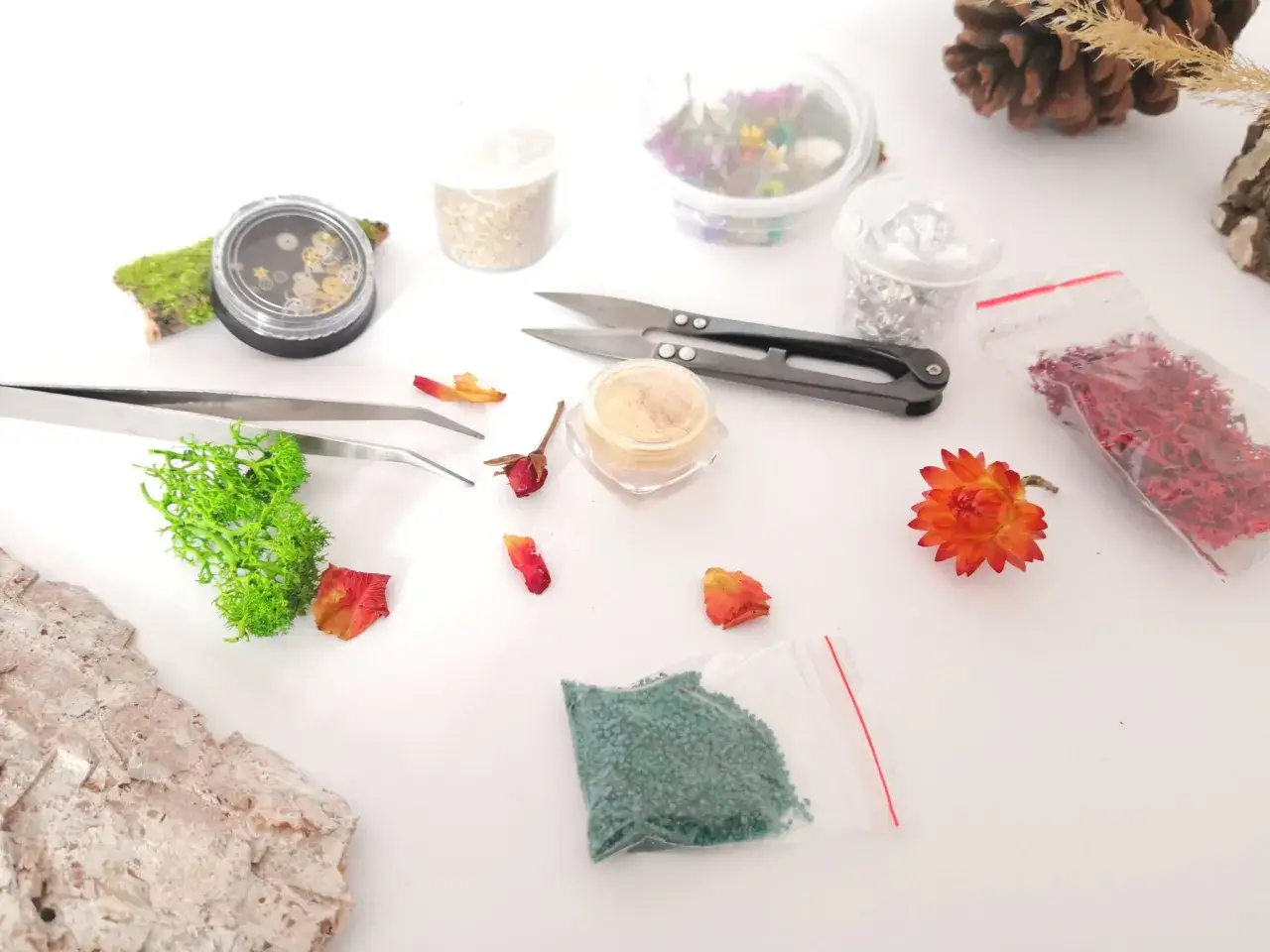 Materiały do tworzenia ozdób z żywicy epoksydowej: mech, suszone kwiaty, brokat, folia, pęseta, nożyczki.