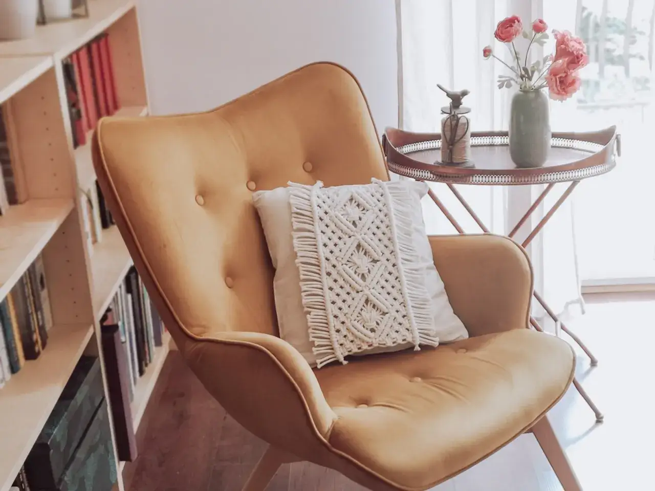 Żółty fotel z poduszką ozdobioną makramą. W tle regał z książkami i stolik z kwiatami. Makrama poduszka krok po kroku.