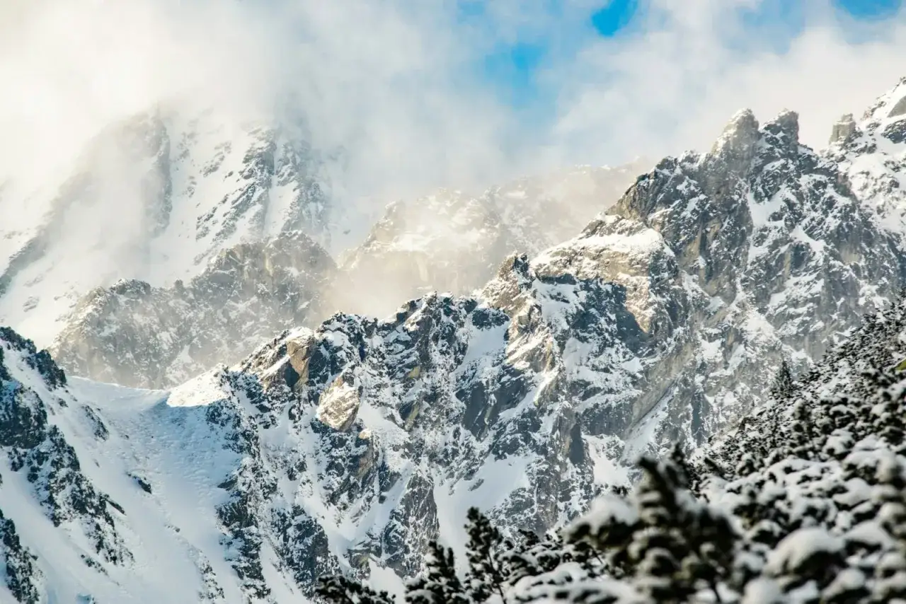 Śnieżne szczyty górskie w słońcu, z mgłą i niebieskim niebem.