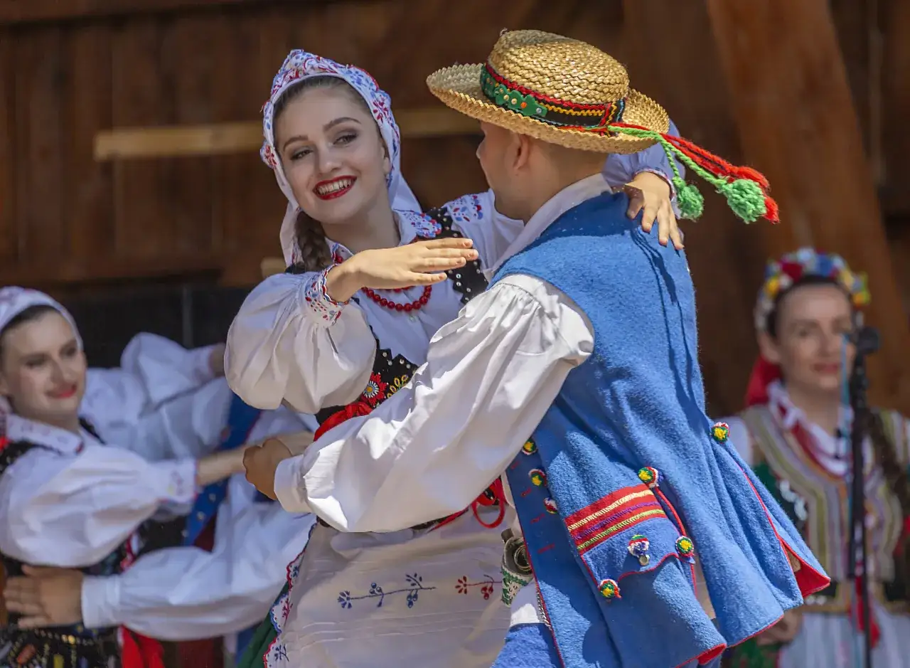 Młoda para w tradycyjnych strojach ludowych, tańcząca w rytm polskiej muzyki.