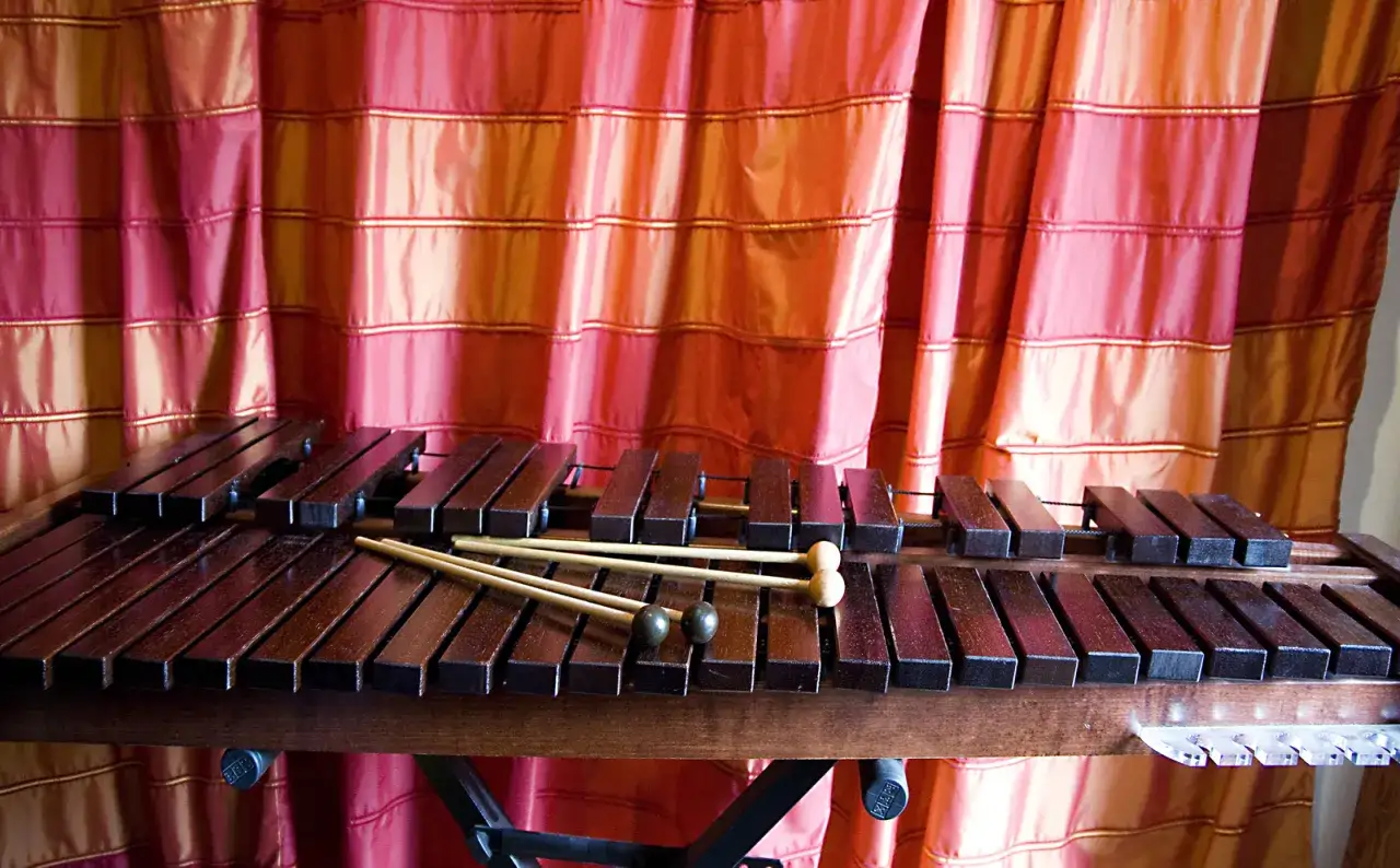 Ksylofon, instrument muzyczny na literę K, z pałeczkami, na tle czerwonej zasłony.