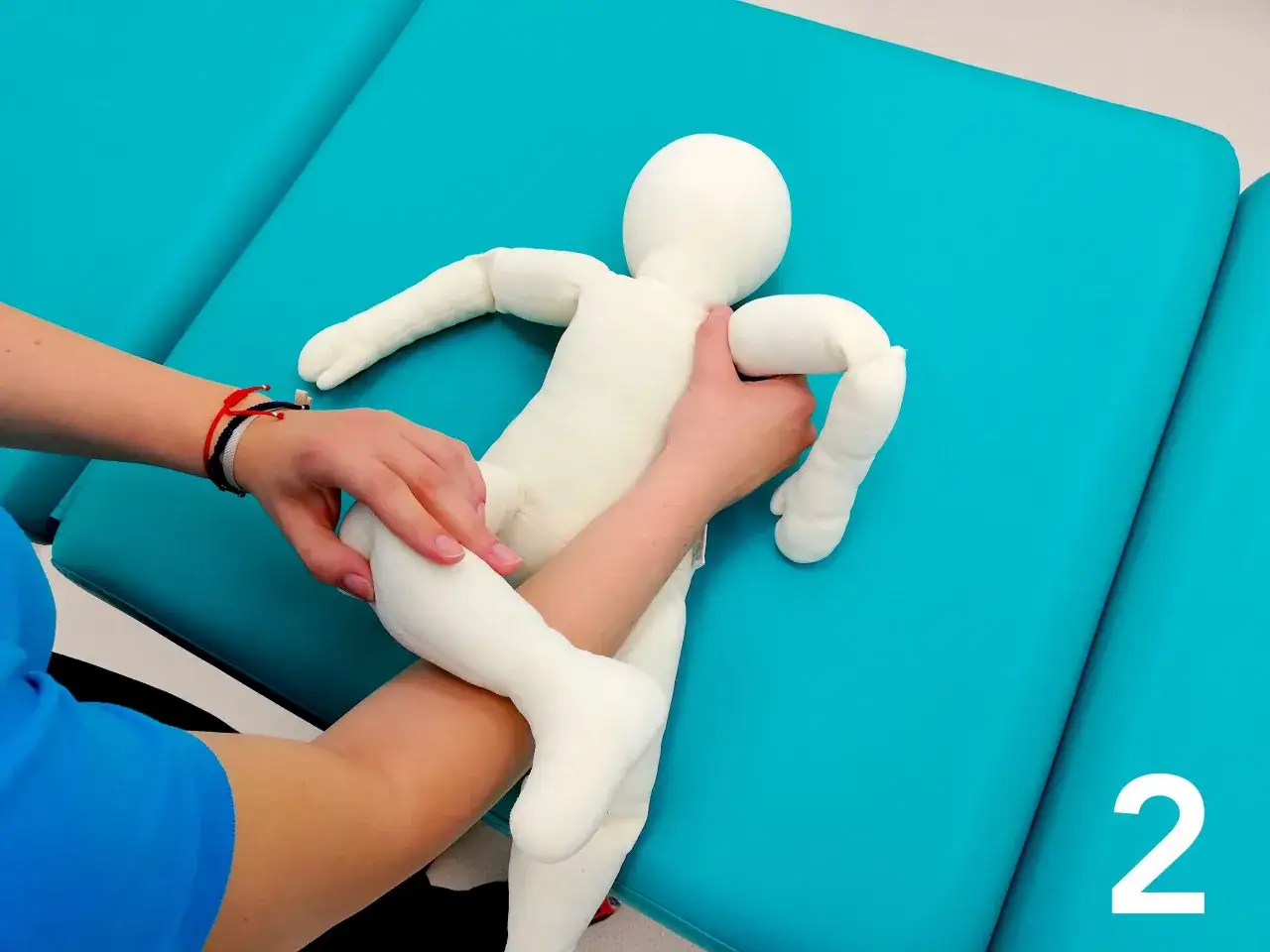 Fizjoterapeuta pokazuje mamie, jak podnosić niemowlę, trzymając pluszową lalkę.