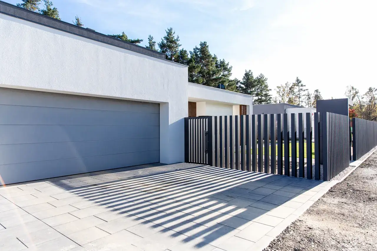 Nowoczesny podjazd bez ogrodzenia, z szarą bramą garażową i pionowym płotem.