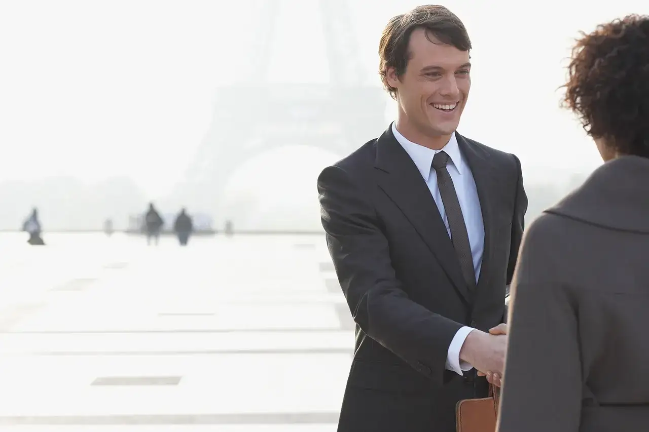 Uśmiechnięty mężczyzna w garniturze wita się z kobietą na tle Wieży Eiffla. Rozmowa o tym, jakich języków warto się uczyć.