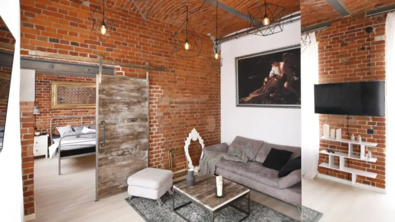 Styl loftowy z ceglanymi ścianami, jak z obrazka. Wnętrze z sypialnią, salonem i telewizorem.