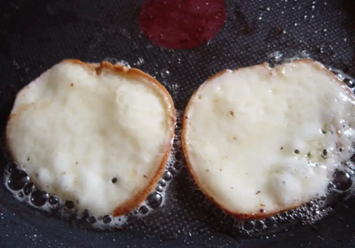 Dwa plastry oscypka smażone na patelni, otoczone bąbelkami oleju.