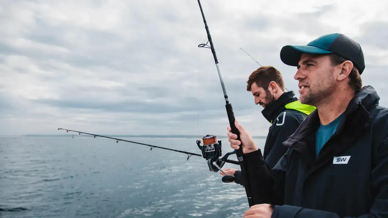 Dwóch mężczyzn łowi ryby na morzu, trzymając wędki spinningowe.
