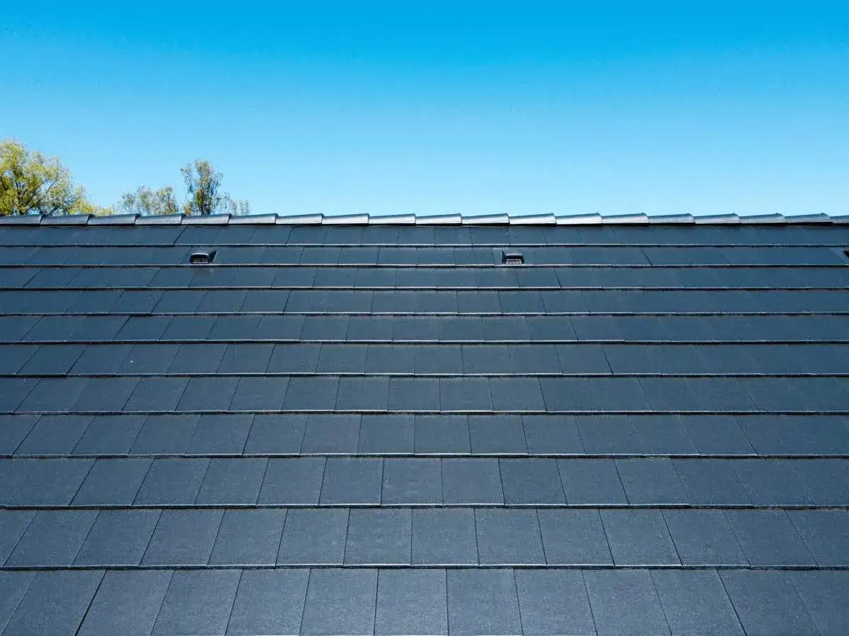 Ciemnoszara dachówka płaska ułożona na mijankę, tworząca równą, nowoczesną powierzchnię dachu pod błękitnym niebem.