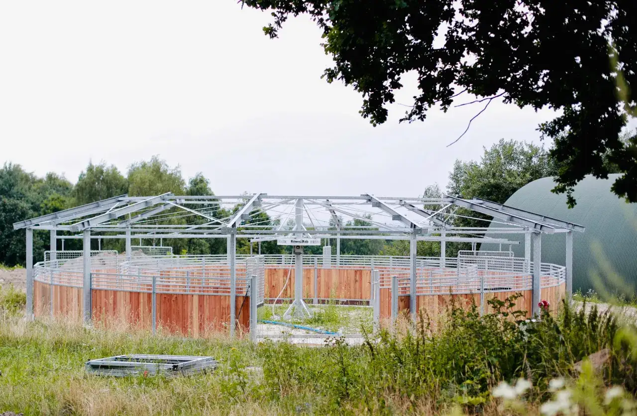 Nowa karuzela dla koni, z drewnianymi ściankami i metalową konstrukcją, czeka na swoich jeźdźców i rumaki.