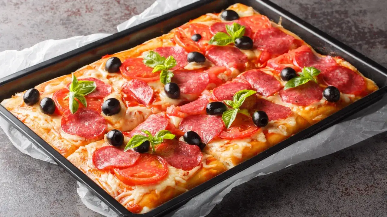 Chrupiąca pizza na cieście francuskim z salami, pomidorami i oliwkami, udekorowana listkami bazylii.