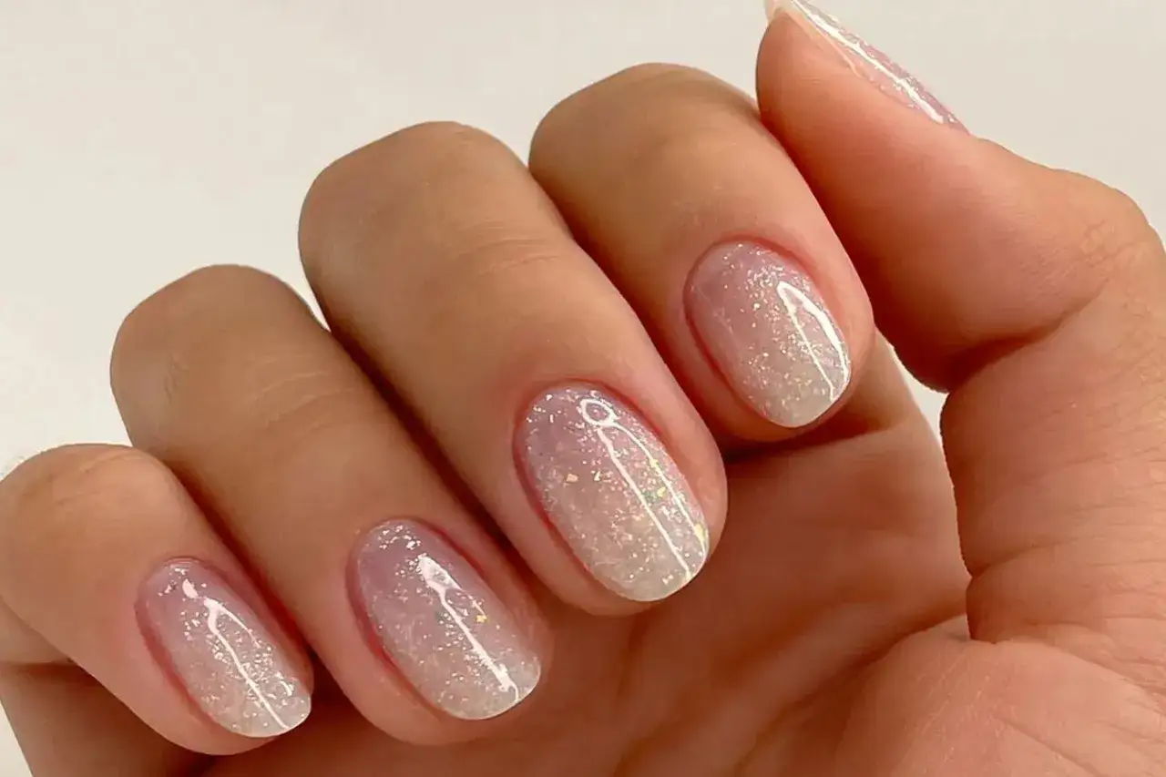 Nahaufnahme einer Hand mit ovalen Nägeln, die mit schimmerndem Glitzer-Nagellack in Pastelltönen verziert sind.