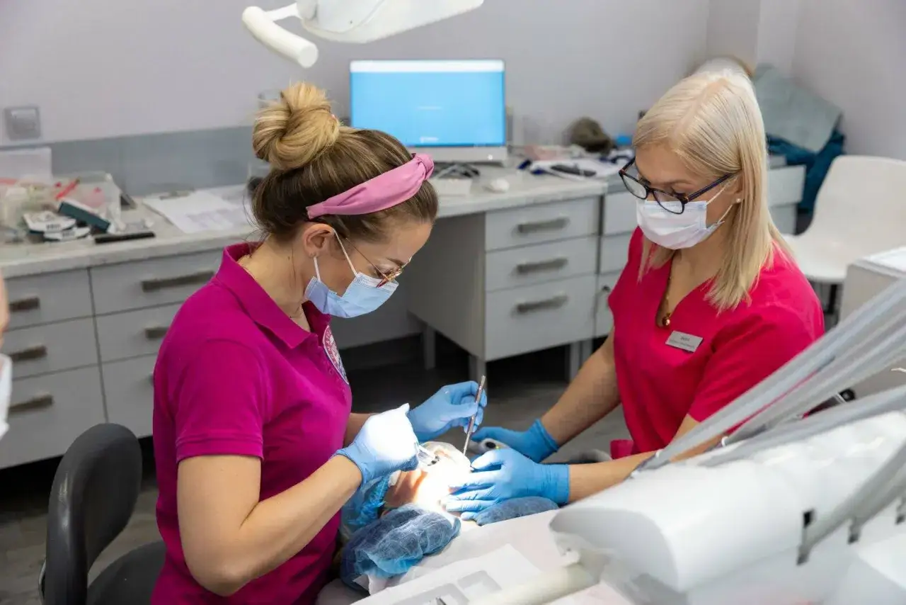 Dwie dentystki w maseczkach i rękawiczkach wykonują zabieg u pacjenta.