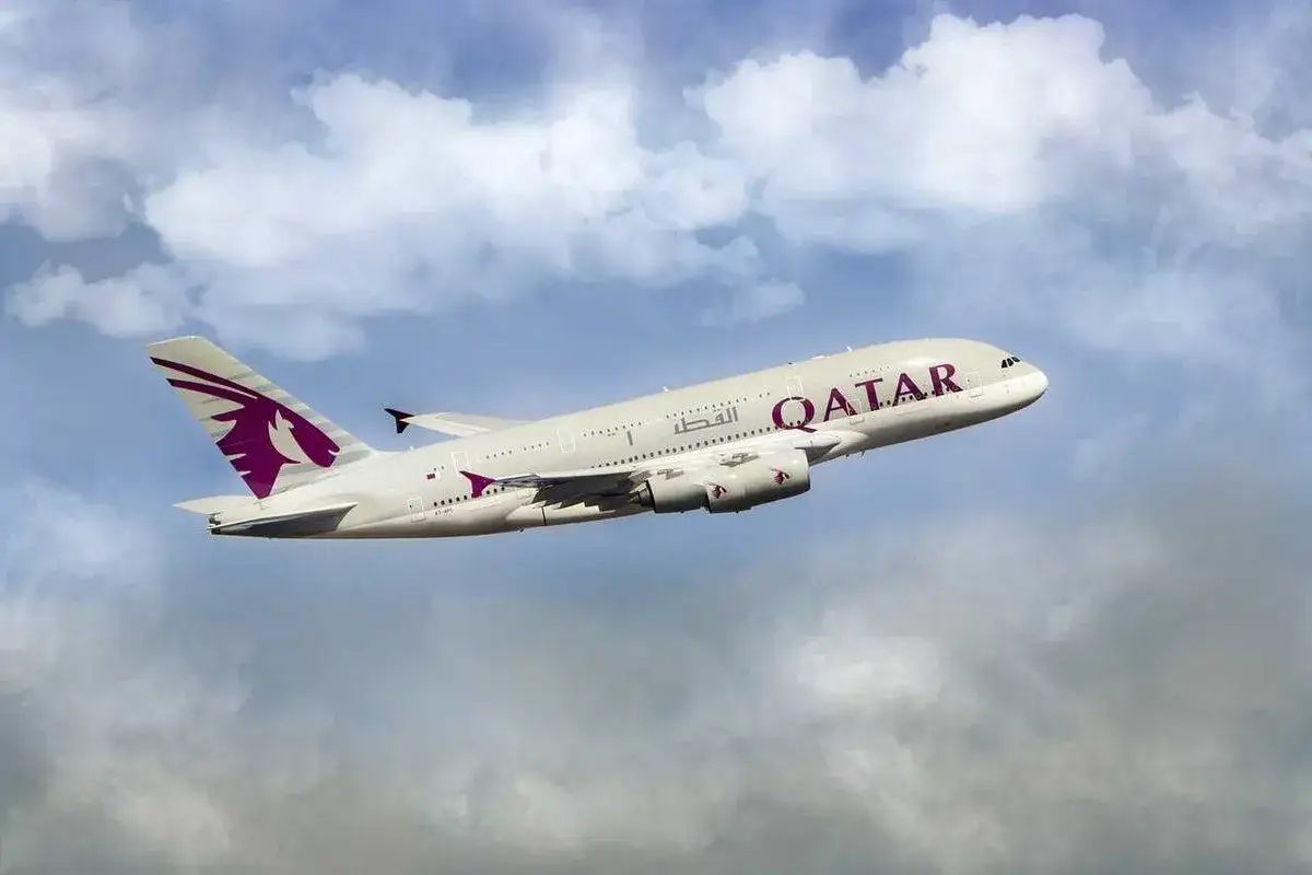 Qatar Airways Airbus A380 airplane in flight against a cloudy blue sky.