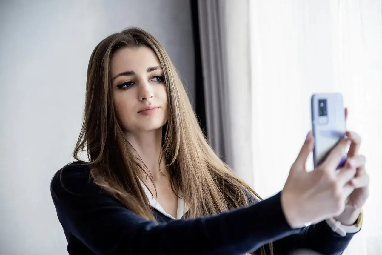 Młoda kobieta robi sobie selfie telefonem, przygotowując się do zrobienia zdjęcia do CV.