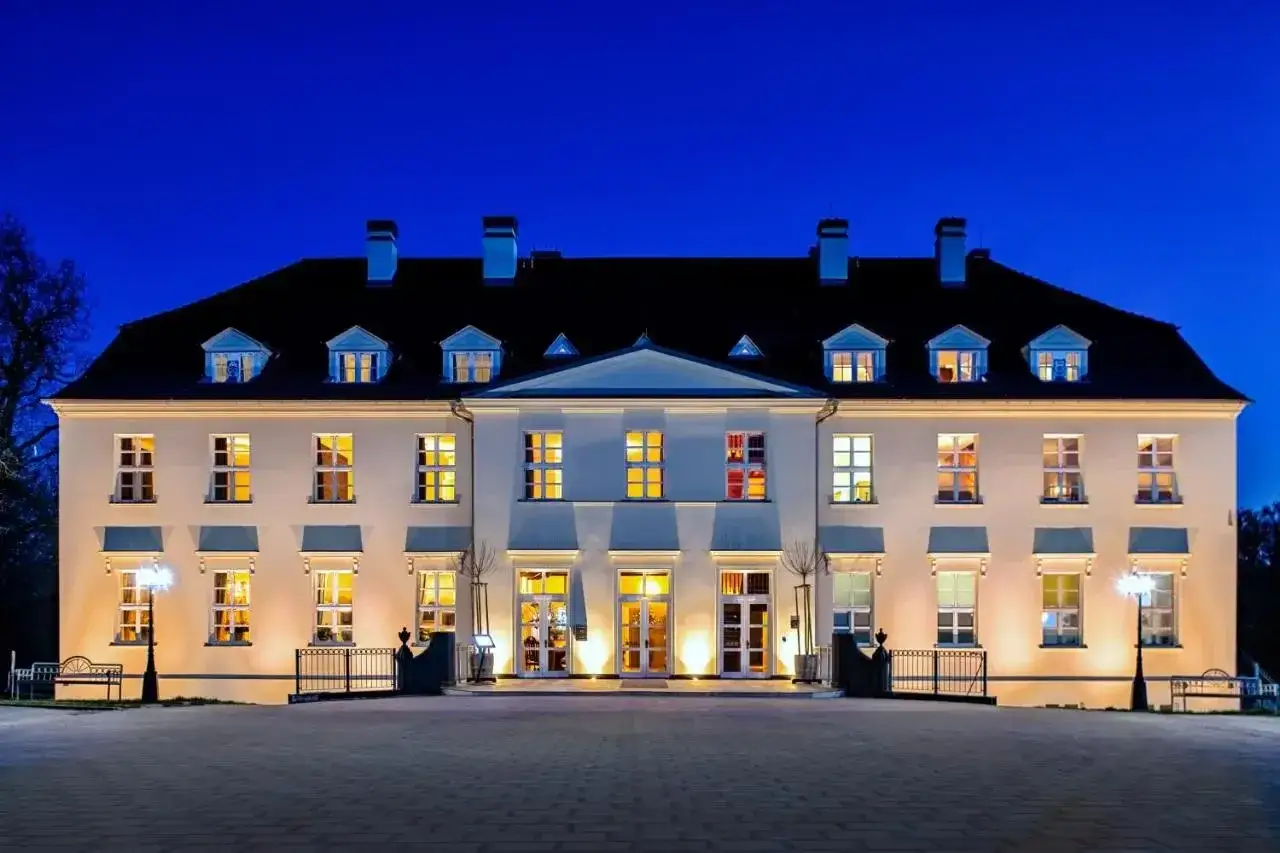 Beleuchtetes Schloss mit vielen Fenstern bei Nacht vor blauem Himmel.