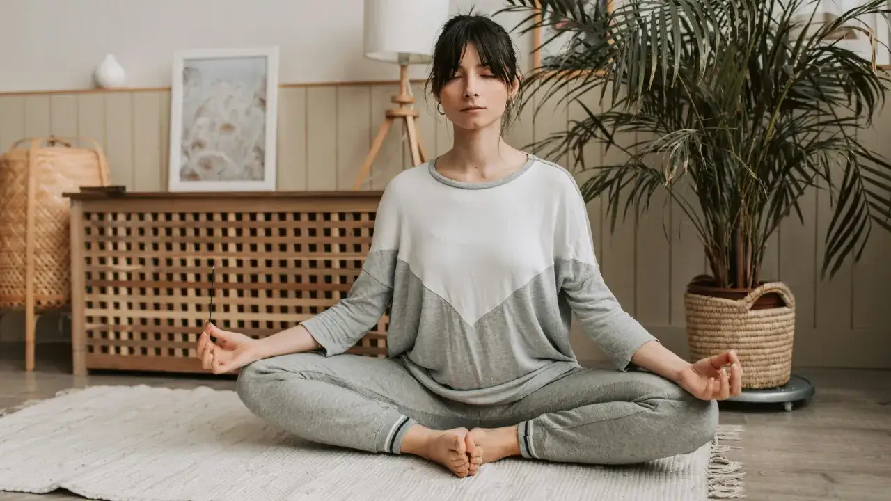 Kobieta medytuje w domu, praktykując slow life. W dłoni trzyma kadzidełko.