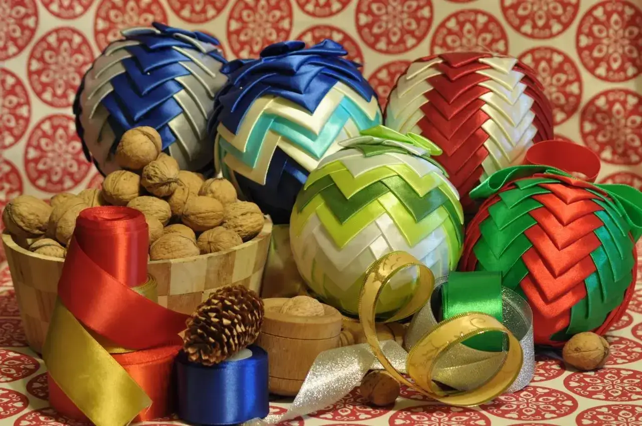 Kolorowe ozdoby ze wstążki satynowej w kształcie kuli, otoczone orzechami i wstążkami.