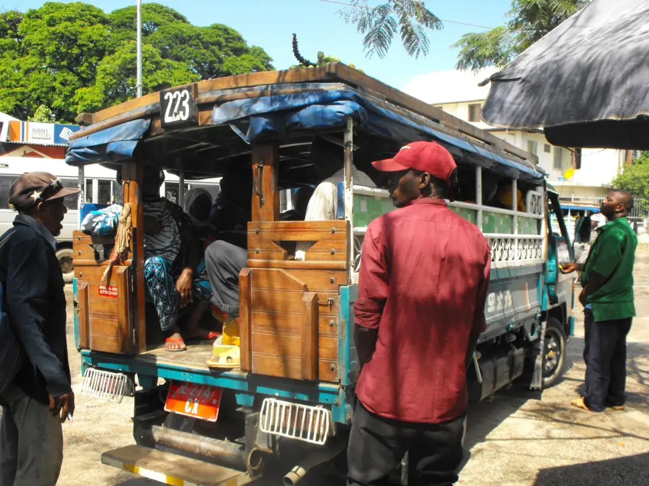 Ludzie wsiadają do dala dala na Zanzibarze. Widać drewnianą konstrukcję pojazdu i pasażerów.