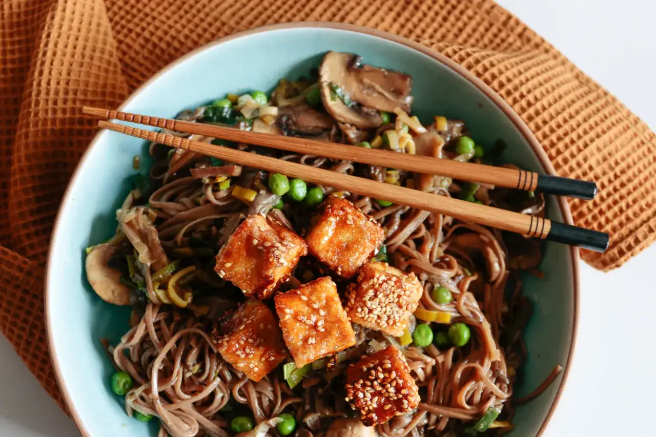 Pyszny makaron z tofu po azjatycku z grzybami i groszkiem, podany z pałeczkami.